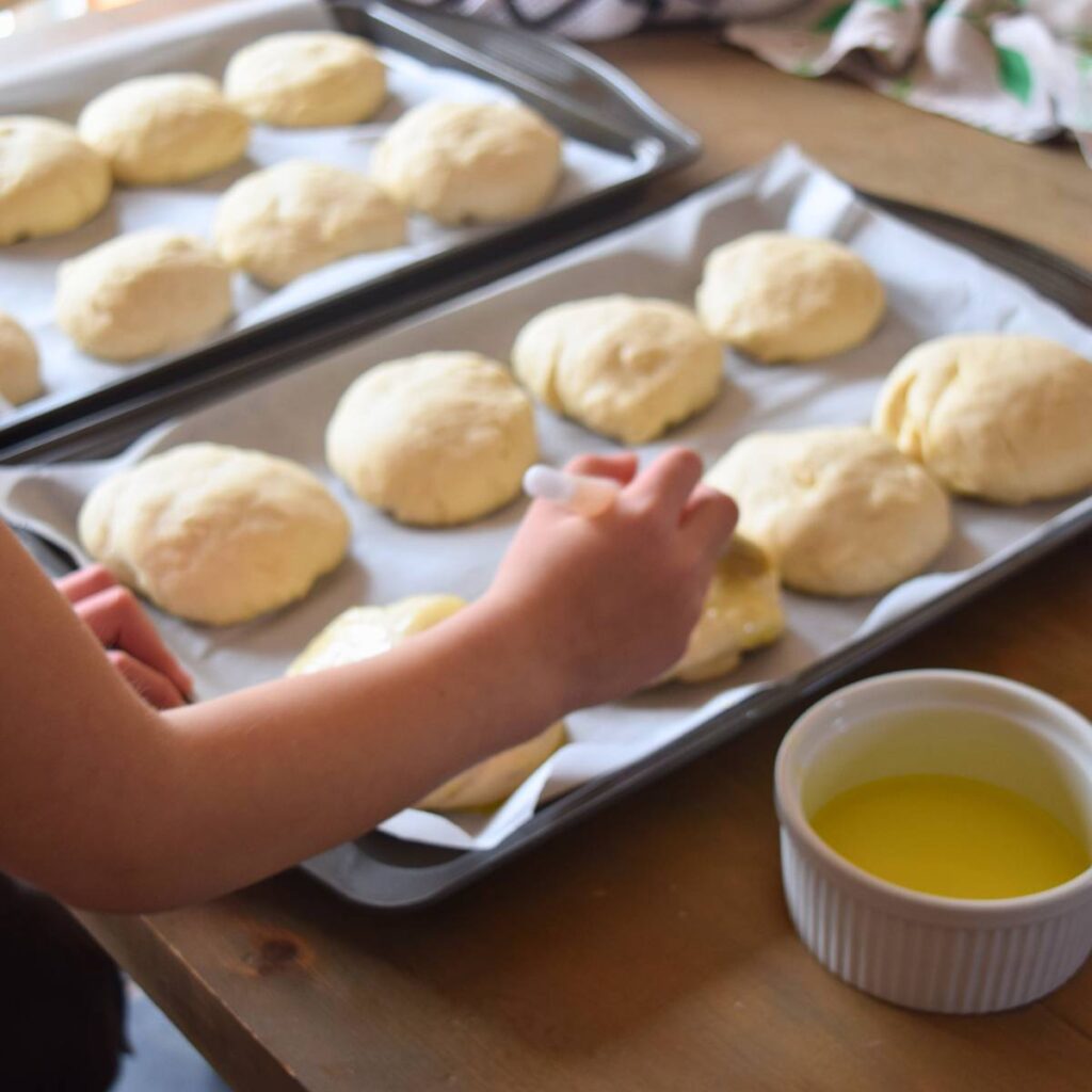 Super Simple Cheesy Buns dough balls on parchment paper being brushed with butter before getting cheese