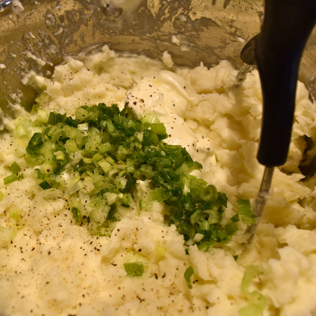 Sour Cream Potato Casserole potatoes being mashed together with sour cream, green onion and salt and pepper